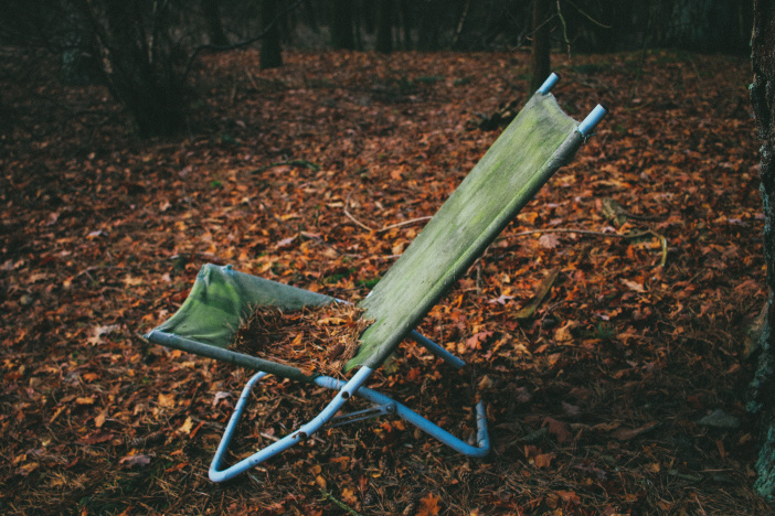 An old lawn chair in the woods, decrepit and covered in leaves